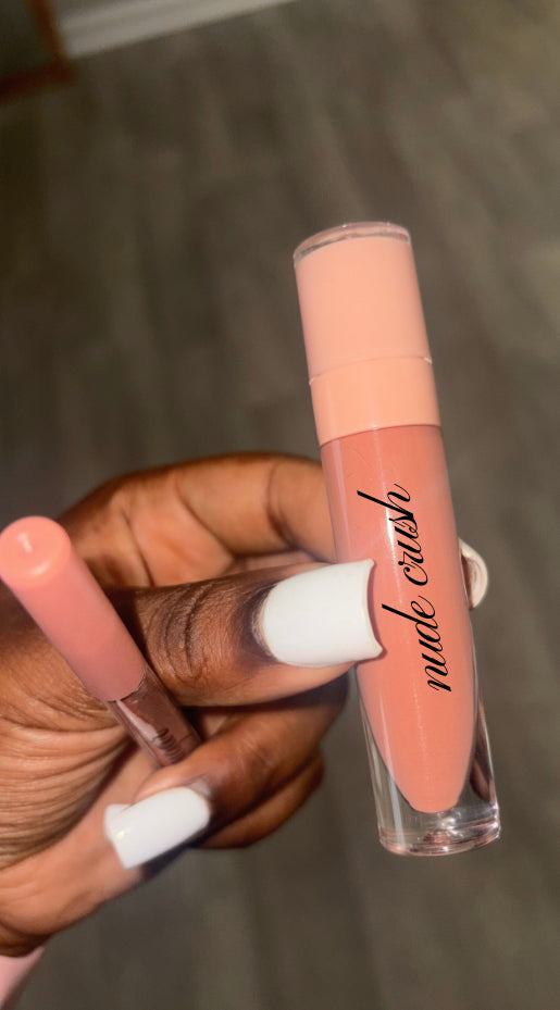 A hand with white nails holds the Sugar rush lip combo—a nude-colored gloss labeled “Nude Crush” and a matching Brown Sugar lip pencil—against a blurred, neutral background, perfectly capturing the look of glossy nude lips.