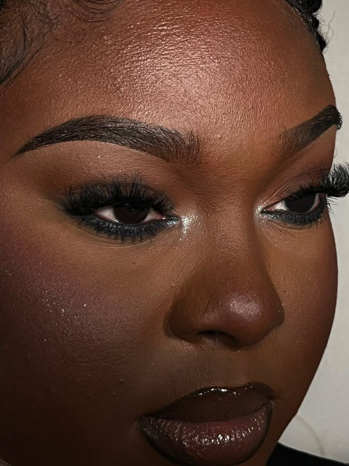 A close-up of a woman's face with smooth, glowing skin, bold eyebrows, dramatic eye makeup featuring Purple Rain lash clusters for customizable volume and long lashes, shimmering eyeshadow, contoured cheeks, and glossy lips.